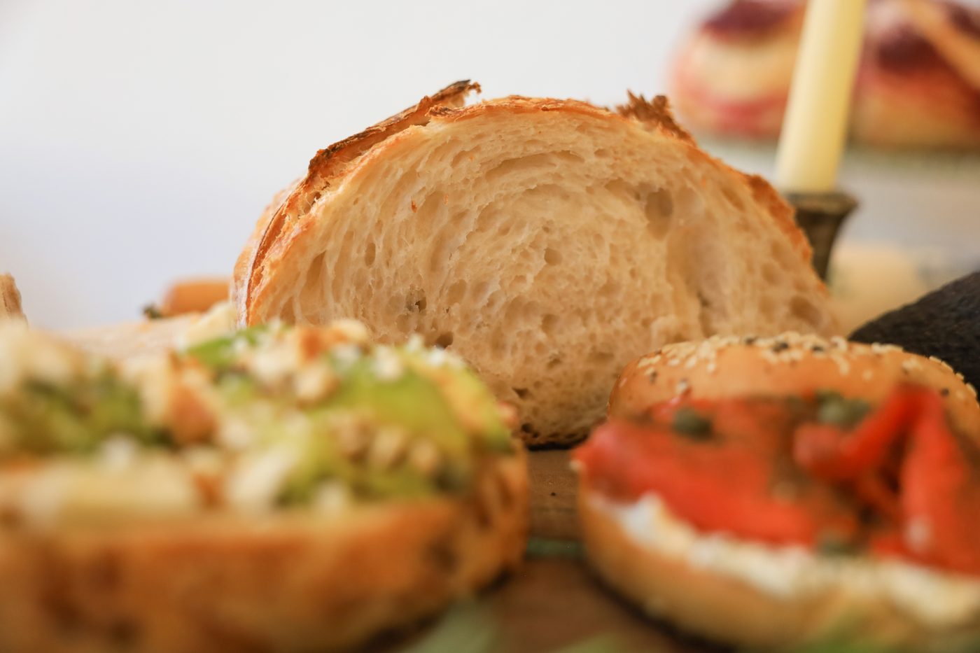 Sourdough toasts and bagels laid out with avocado, tomato, and herbs